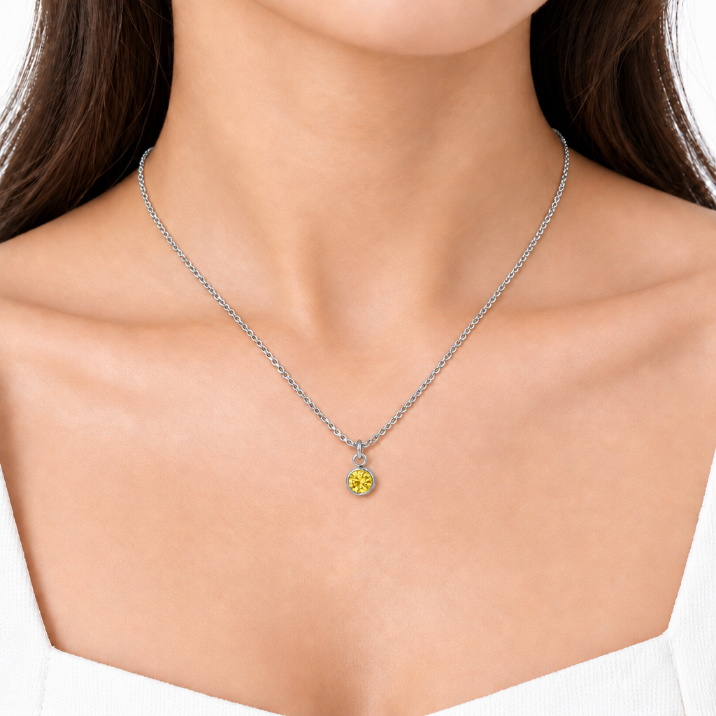 Modelka prezentuje srebrzysty naszyjnik z okrągłą żółtą cyrkonią